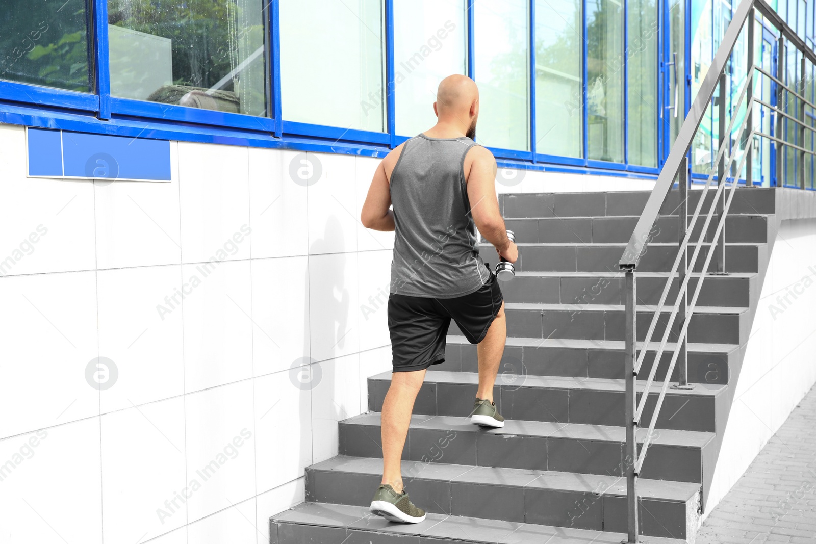 Photo of Overweight man running with dumbbells on stairs outdoors