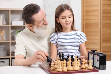 Senior man teaching his granddaughter to play chess at home