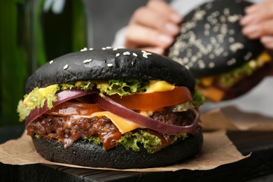 Photo of Tasty burger with black buns and woman eating on background
