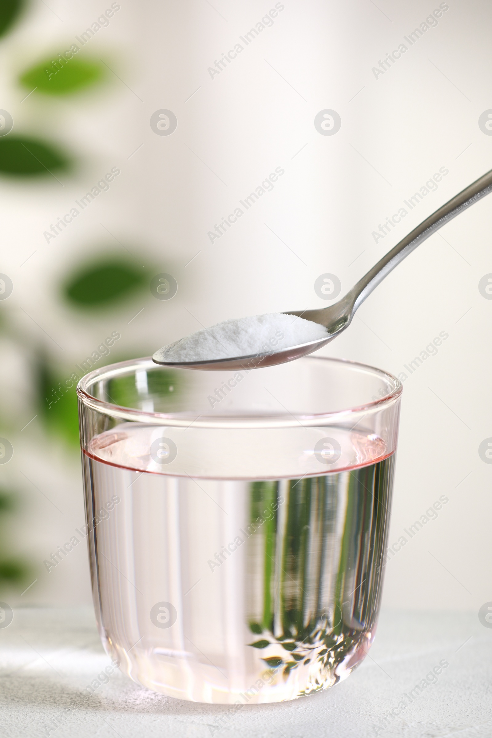 Photo of Spoon with baking soda over glass of water at white table against blurred background