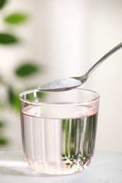 Photo of Spoon with baking soda over glass of water at white table against blurred background