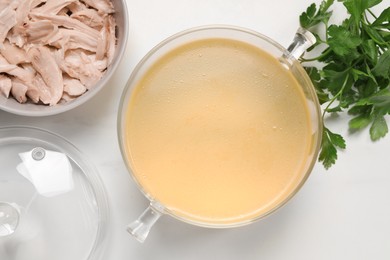 Photo of Glass pot with tasty bouillon, chicken and parsley on white marble table, flat lay