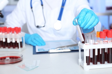 Laboratory worker taking test tube with sample from rack on table, closeup. Research and analysis