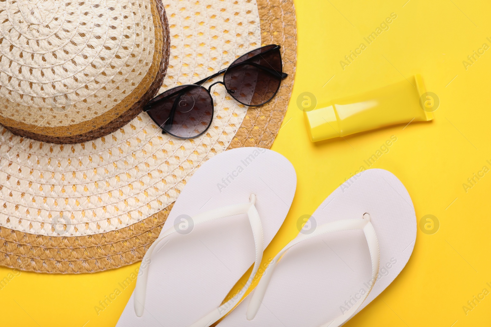 Straw hat, stylish sunglasses, flip flops and sunscreen on yellow background, flat lay. Beach accessories Photo of Straw hat, stylish sunglasses, flip flops and sunscreen on yellow background, flat lay. Beach accessories