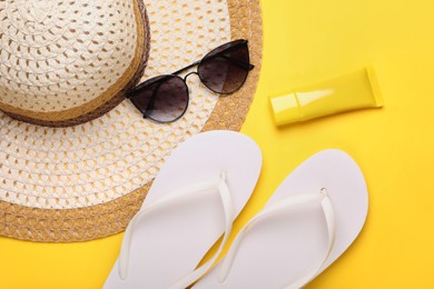 Photo of Straw hat, stylish sunglasses, flip flops and sunscreen on yellow background, flat lay. Beach accessories
