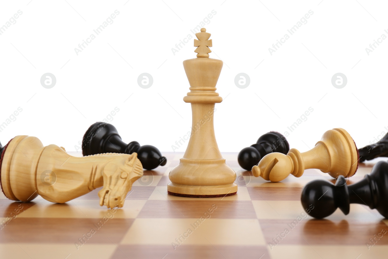 Photo of King among fallen chess pieces on wooden board against white background