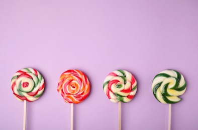 Photo of Many colorful lollipops on violet background, flat lay. Space for text