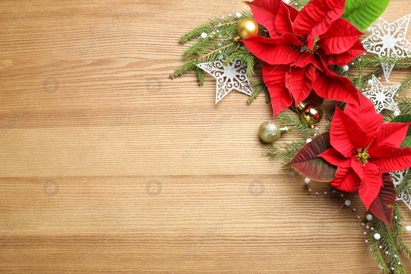 Photo of Flat lay composition with poinsettias (traditional Christmas flowers) and holiday decor on wooden table. Space for text