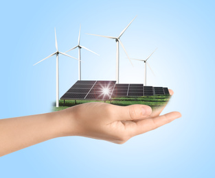 Woman demonstrating solar panel and wind turbines on light blue background, closeup. Alternative energy source 