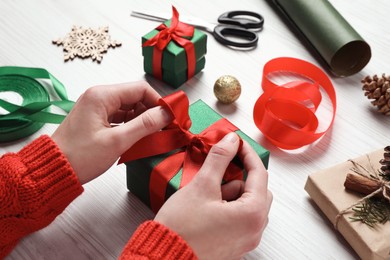 Photo of Christmas present. Woman tying ribbon bow on gift box at white wooden table, closeup