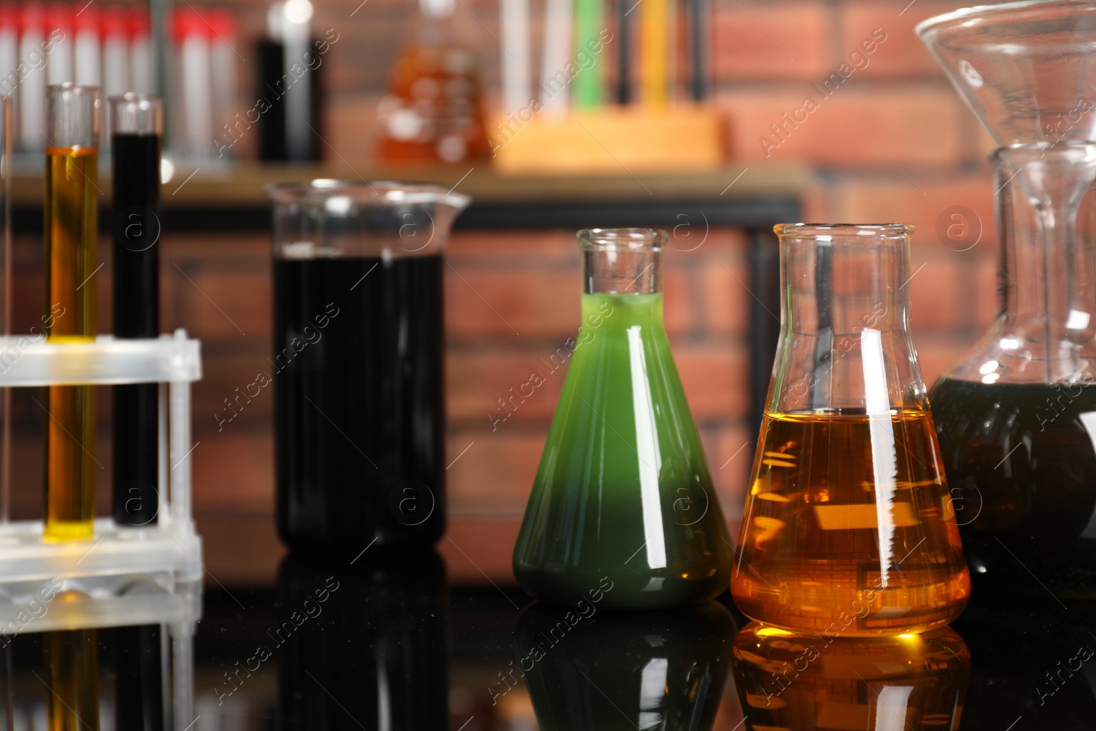 Photo of Laboratory glassware with different types of oil on mirror table indoors, closeup