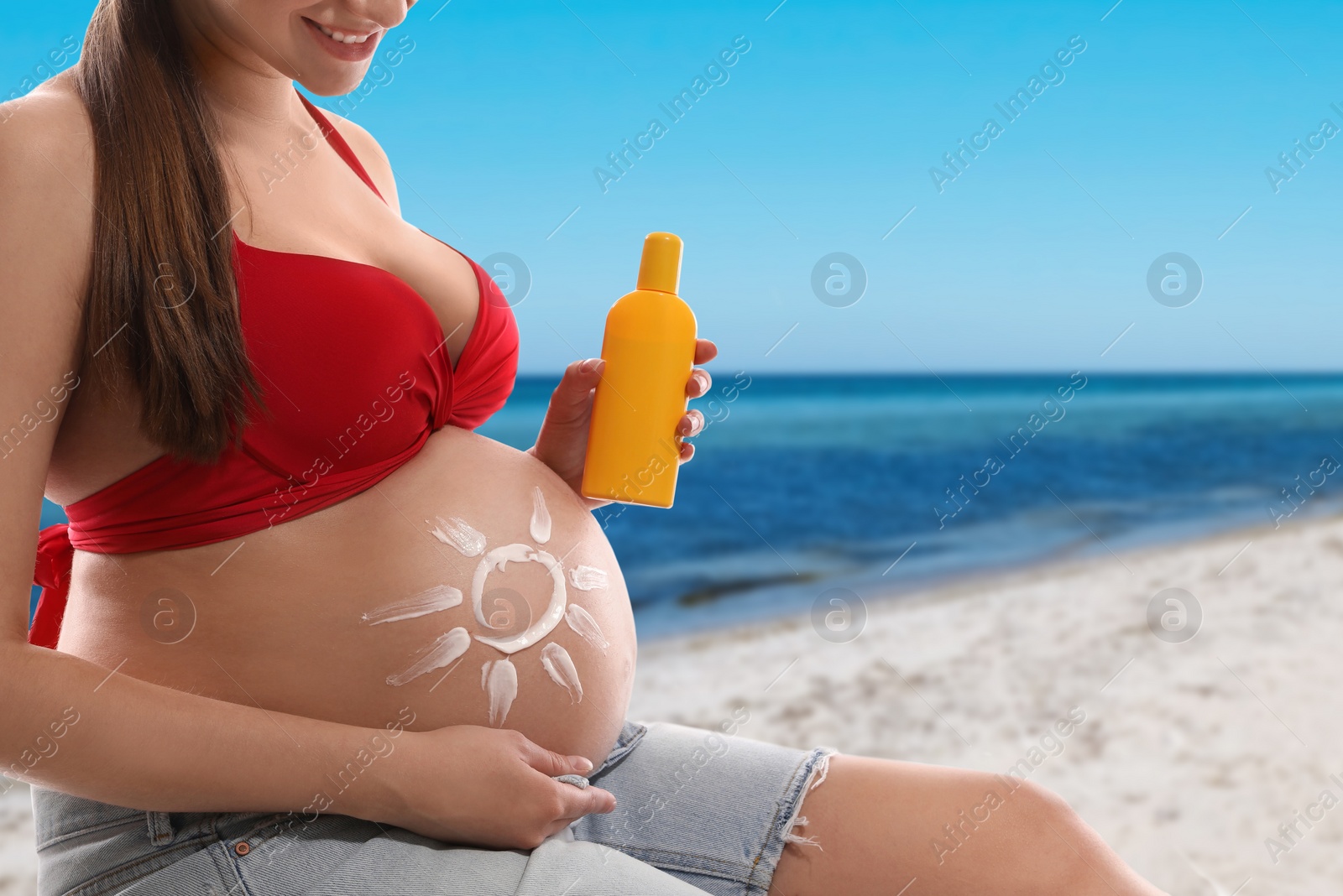 Image of Young pregnant woman with sun protection cream on beach, closeup