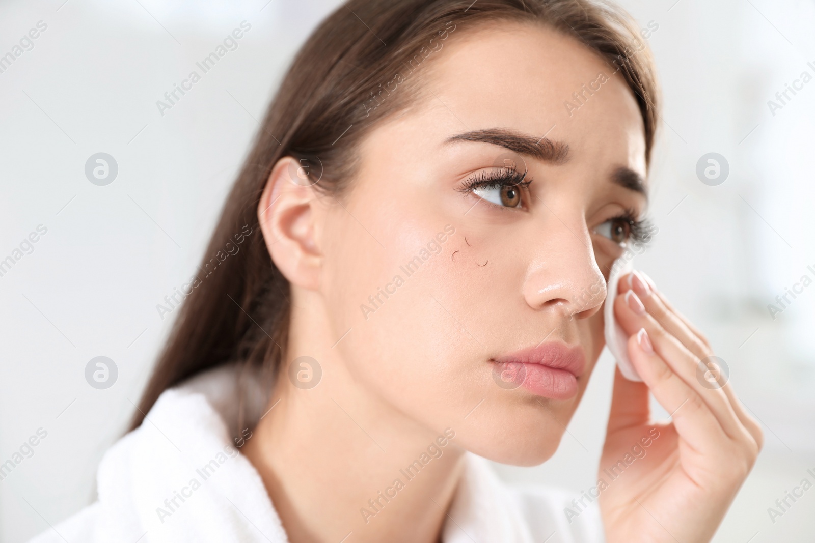 Photo of Young woman with eyelash loss problem removing makeup indoors