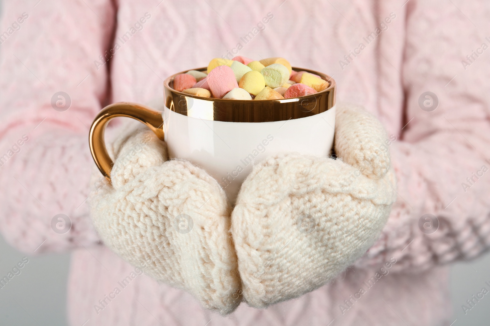 Photo of Woman in knitted mittens holding cup of delicious hot chocolate with marshmallows, closeup