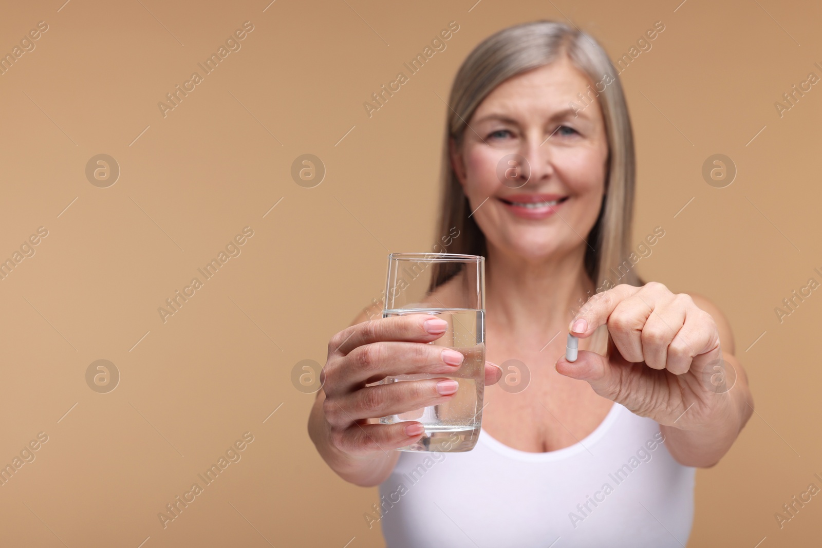 Photo of Beautiful woman with vitamin capsule and glass of water on beige background, selective focus. Space for text