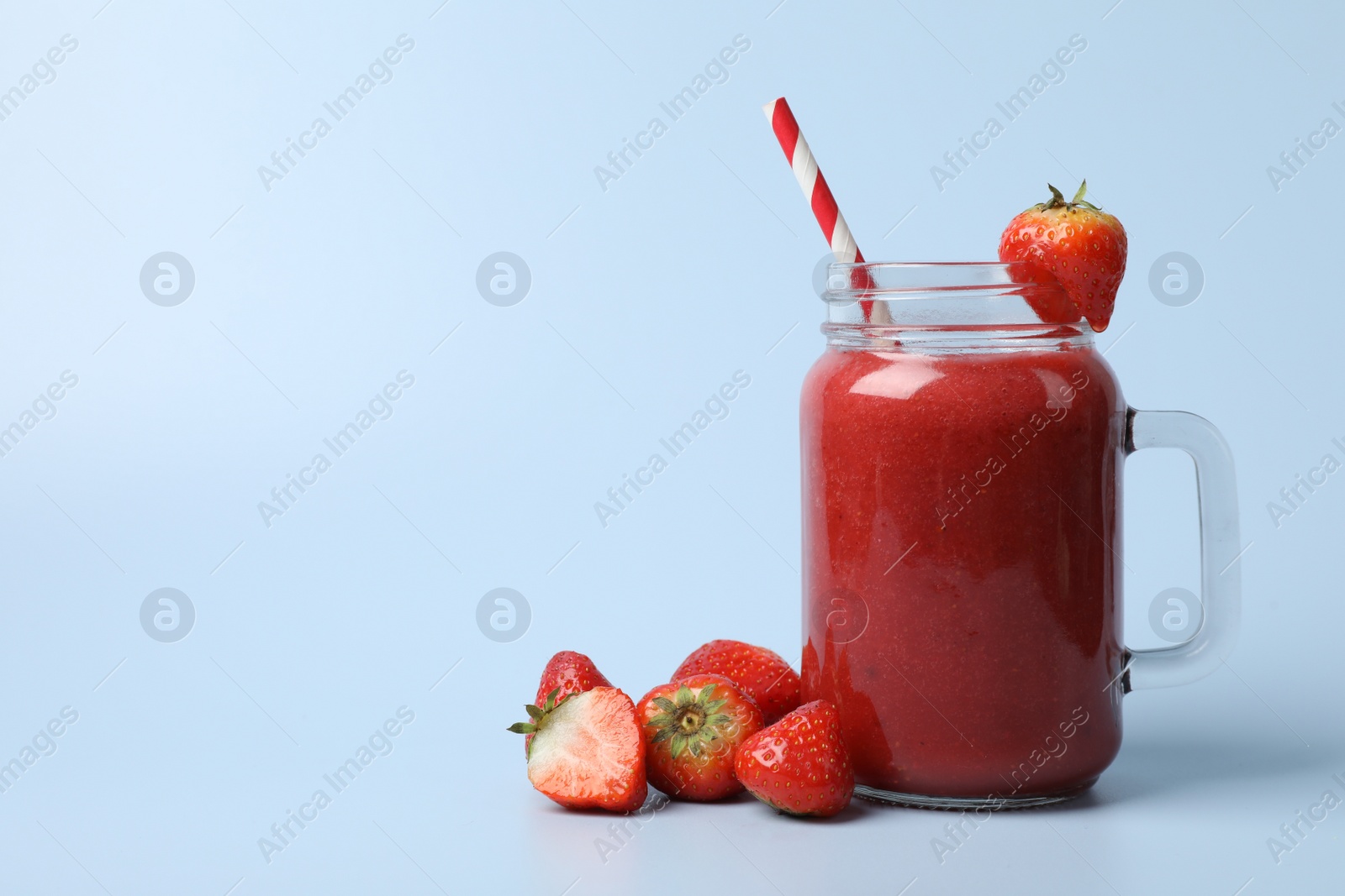 Photo of Mason jar with delicious strawberry smoothie and fresh berries on light blue background. Space for text