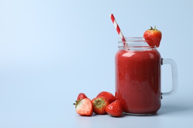 Mason jar with delicious strawberry smoothie and fresh berries on light blue background. Space for text