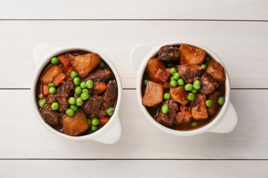 Delicious beef stew with carrots, peas and potatoes on white wooden table, flat lay