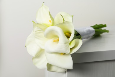Photo of Beautiful calla lily flowers tied with ribbon on white chest of drawers indoors