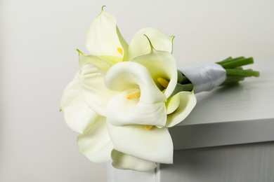 Beautiful calla lily flowers tied with ribbon on white chest of drawers indoors