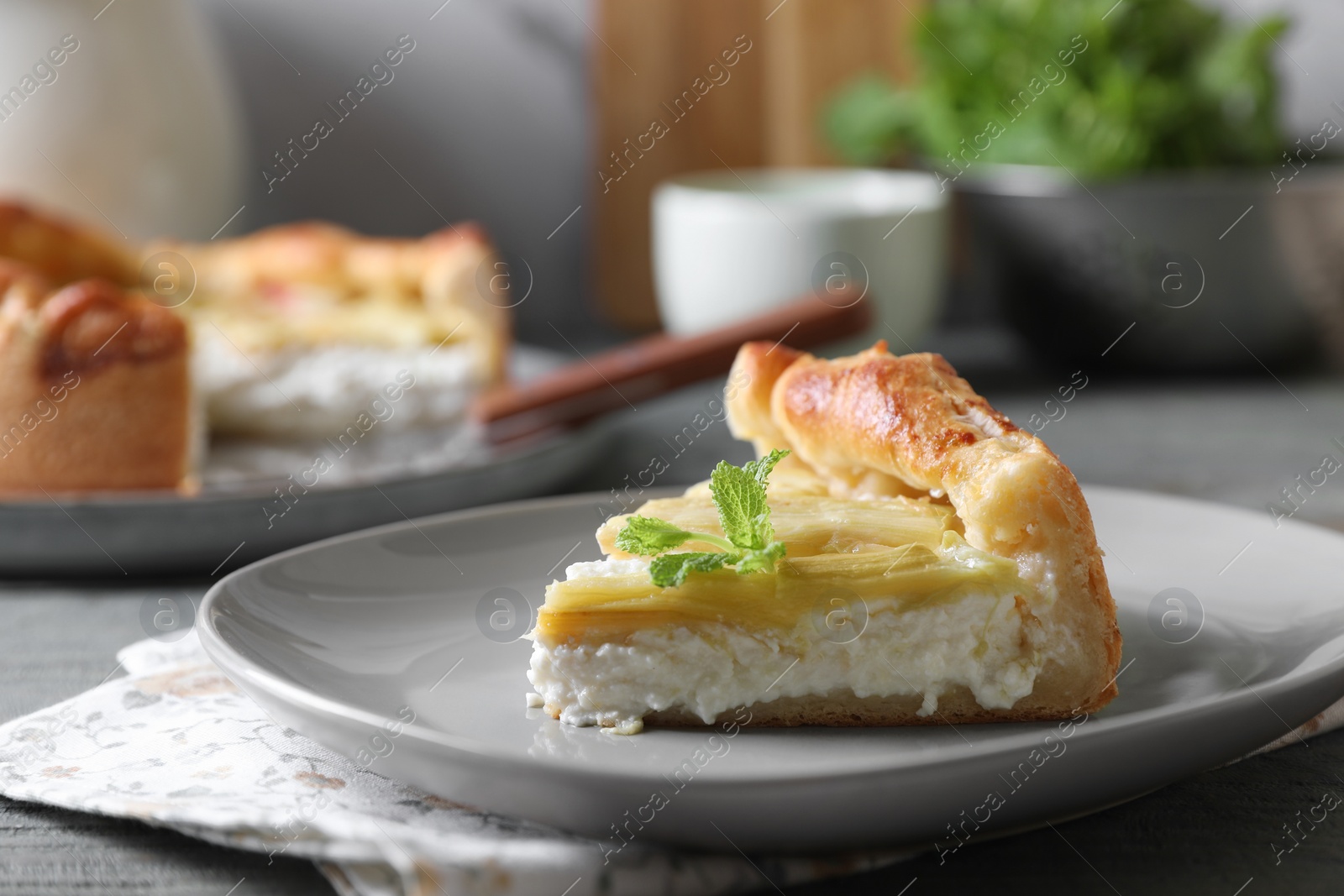 Photo of Piece of freshly baked rhubarb pie with cream cheese and mint leaves on grey wooden table, closeup