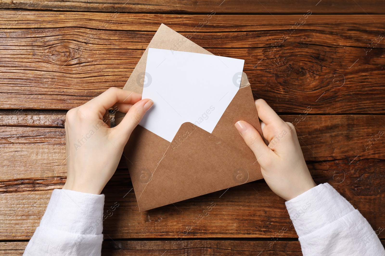 Photo of Woman taking card out of letter envelope at wooden table, top view