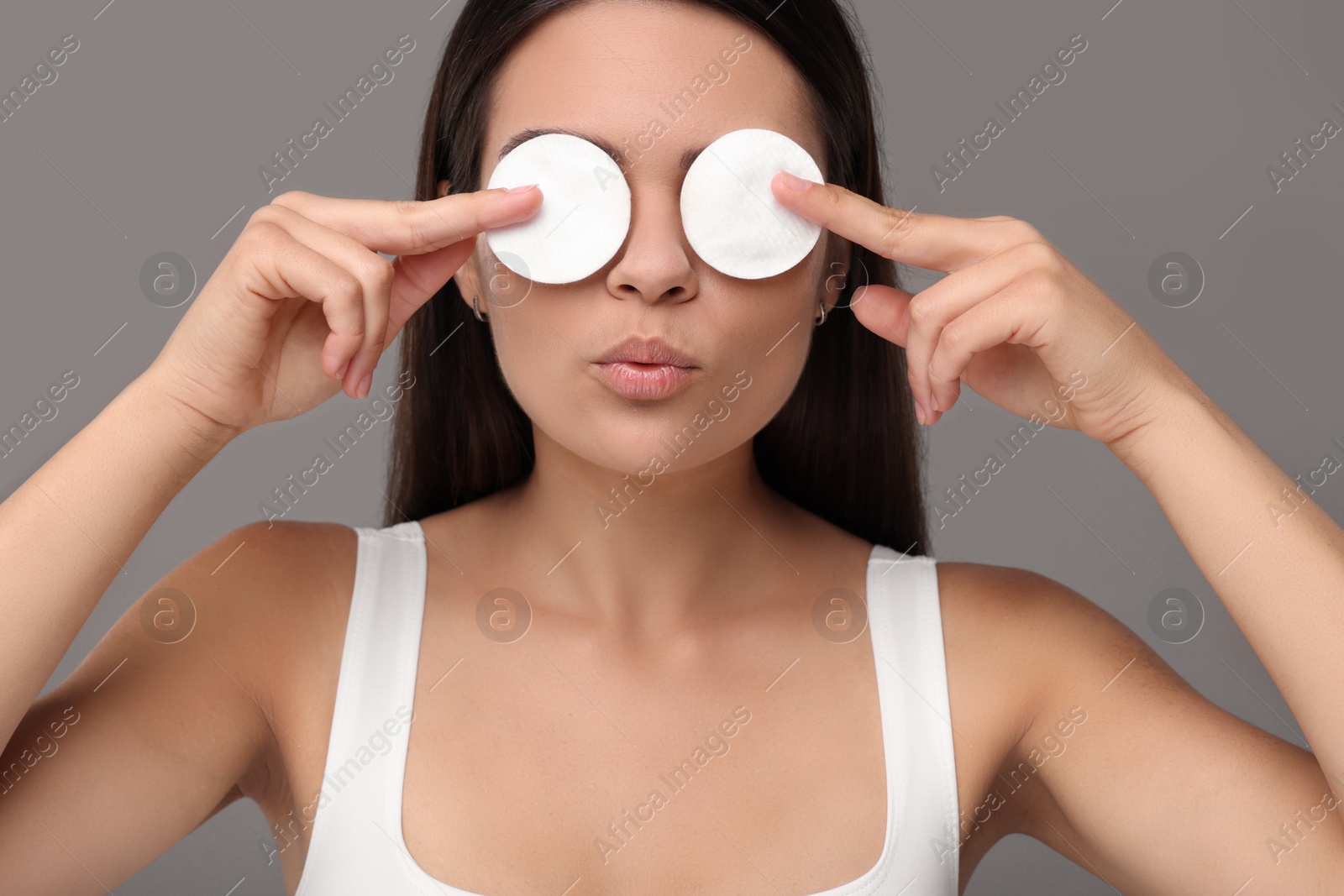 Photo of Young woman covering her eyes with cotton pads on grey background