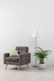 Photo of Stylish living room interior with comfortable armchair, houseplant and lamp near white wall indoors