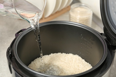 Photo of Water pouring into modern rice cooker in kitchen