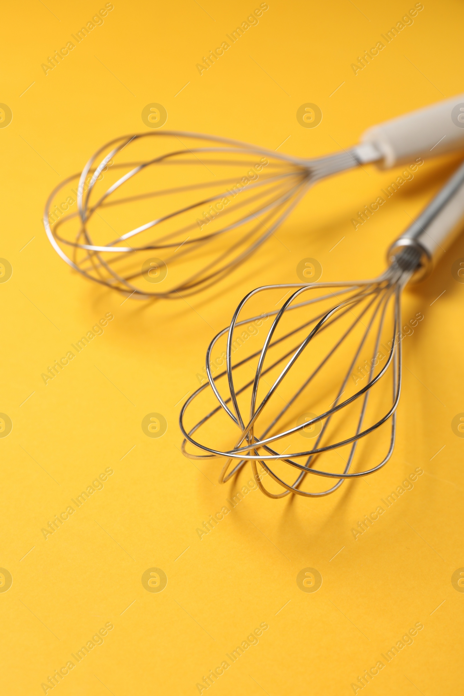 Photo of Two metal whisks on yellow background, closeup
