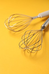 Photo of Two metal whisks on yellow background, closeup