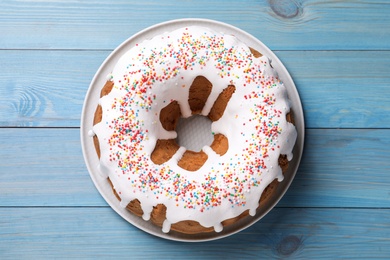 Photo of Glazed Easter cake with sprinkles on light blue wooden table, top view
