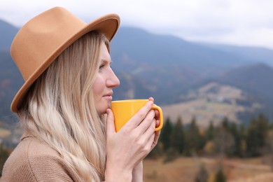 Photo of Young woman with mug of hot drink in mountains. Space for text