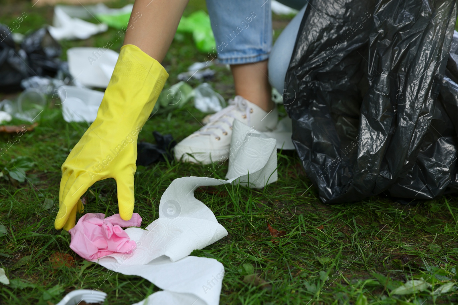 Photo of Woman with plastic bag collecting garbage on green grass outdoors, closeup