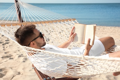 Photo of Young man reading book in hammock on beach