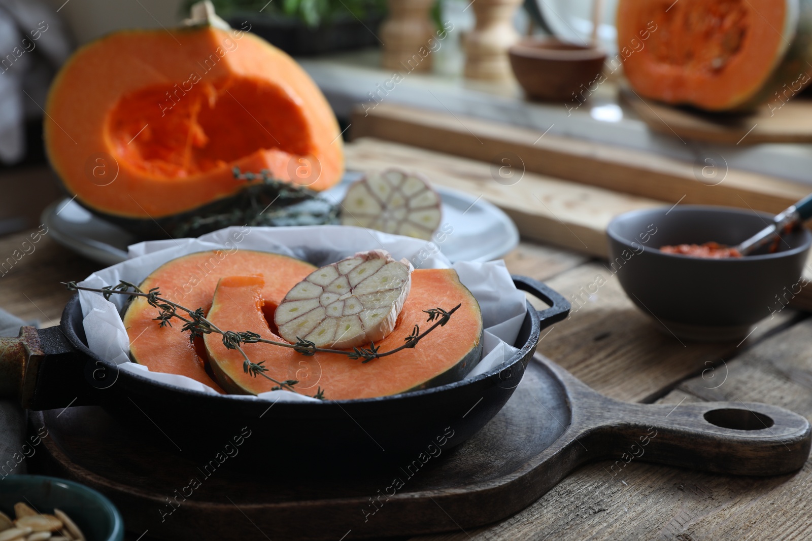Photo of Fresh pumpkin slices with aromatic thyme and garlic in frying pan on wooden table in kitchen