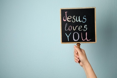 Photo of Woman holding chalkboard with words JESUS LOVES YOU on color background, closeup. Space for text