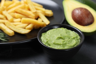 Plate with french fries, guacamole dip and avocado served on black table, closeup