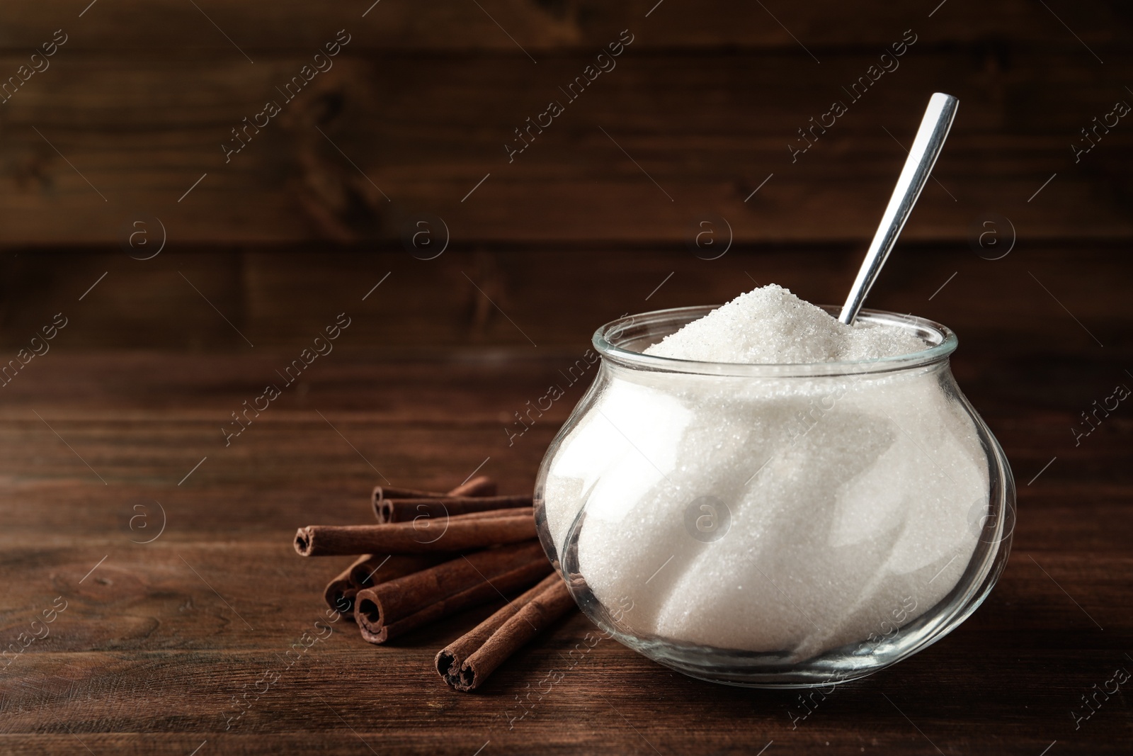 Photo of Glass bowl with sugar and cinnamon on wooden table. Space for text