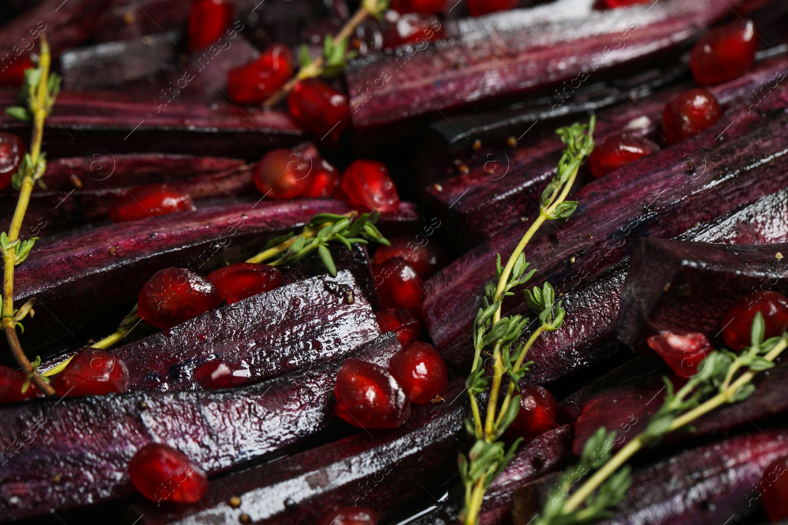 Photo of Raw cut black carrot with pomegranate seeds and thyme as background, closeup