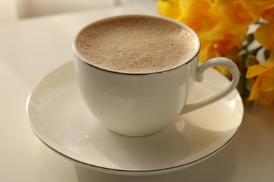 Photo of Delicious morning coffee and flowers on white table, closeup