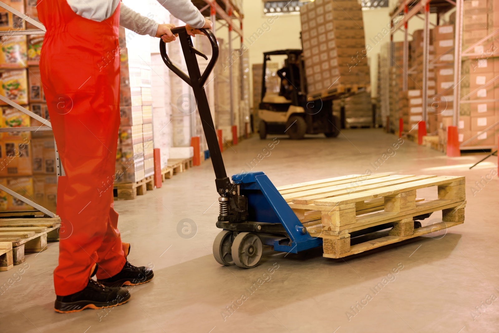 Image of Worker moving wooden pallets with manual forklift in warehouse, closeup