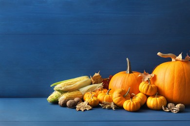 Thanksgiving day. Composition with pumpkins, leaves, walnuts and corn cobs on blue wooden table, space for text