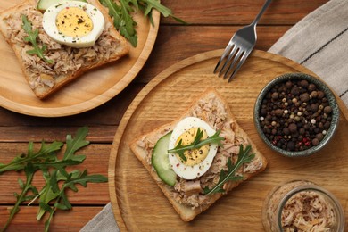 Photo of Delicious sandwiches with tuna, greens, cucumber, boiled egg and ingredients on wooden table, flat lay