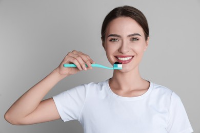 Photo of Young woman holding toothbrush with charcoal toothpaste on grey background