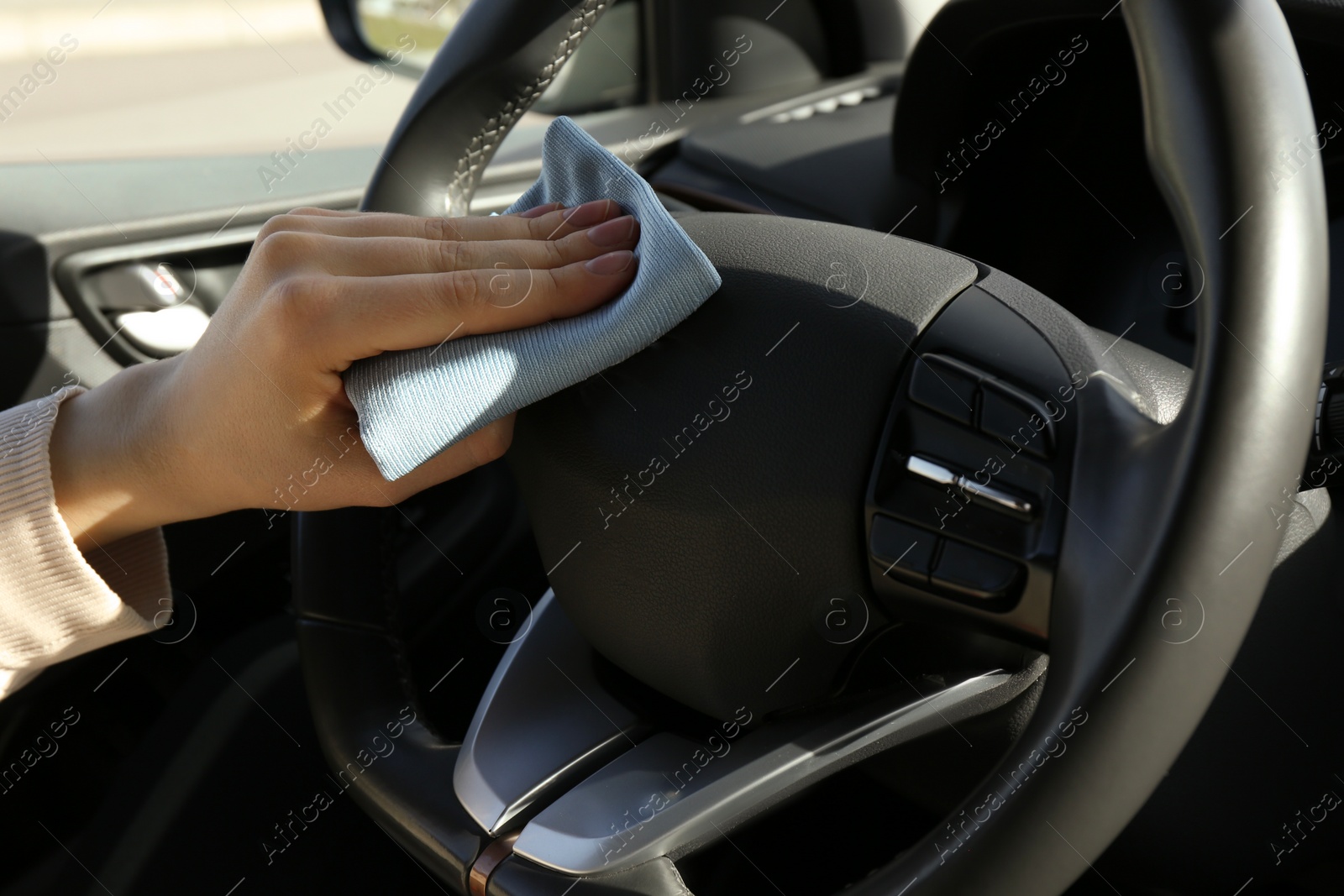 Photo of Woman cleaning steering wheel with rag in car, closeup