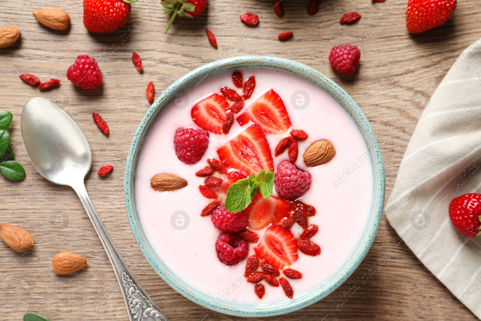 Photo of Smoothie bowl with goji berries and spoon on wooden table, flat lay