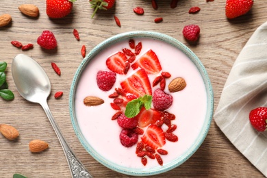 Smoothie bowl with goji berries and spoon on wooden table, flat lay