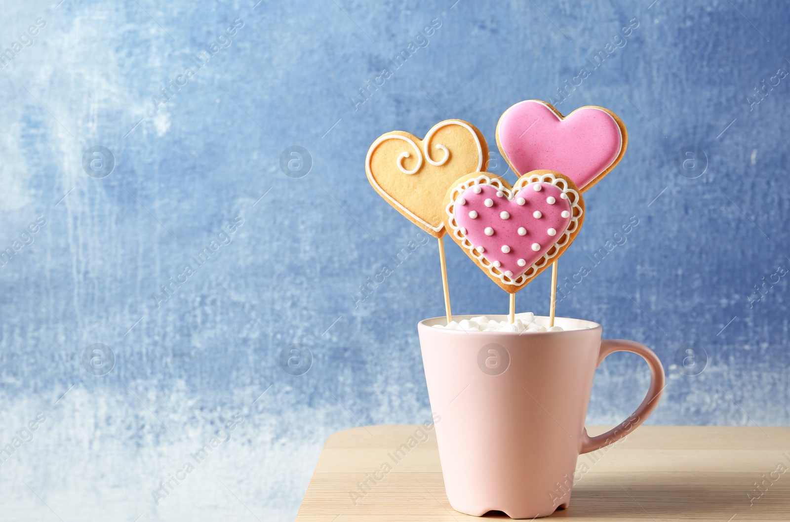 Photo of Decorated heart shaped cookie pops in cup on table. Space for text