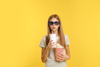 Emotional teenage girl with 3D glasses, popcorn and beverage during cinema show on color background